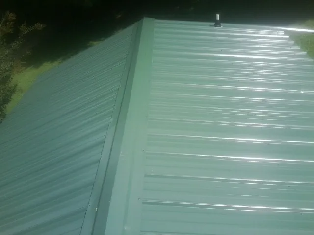 New green metal panels meeting at the ridge of a roof — Flat Roof Repair work by our crew in Morristown