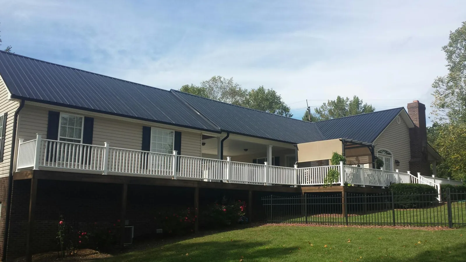 Black metal roof above a long white railed deck on a hillside home in Morristown
